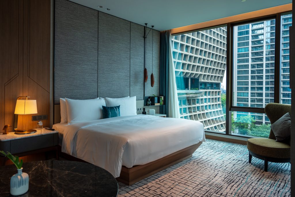 A hotel room with a chair and a bed at dusk.